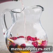 A glass pitcher filled with peach slices and raspberries and rose wine pouring in.