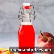Homemade peach syrup in a bottle with fresh peaches.