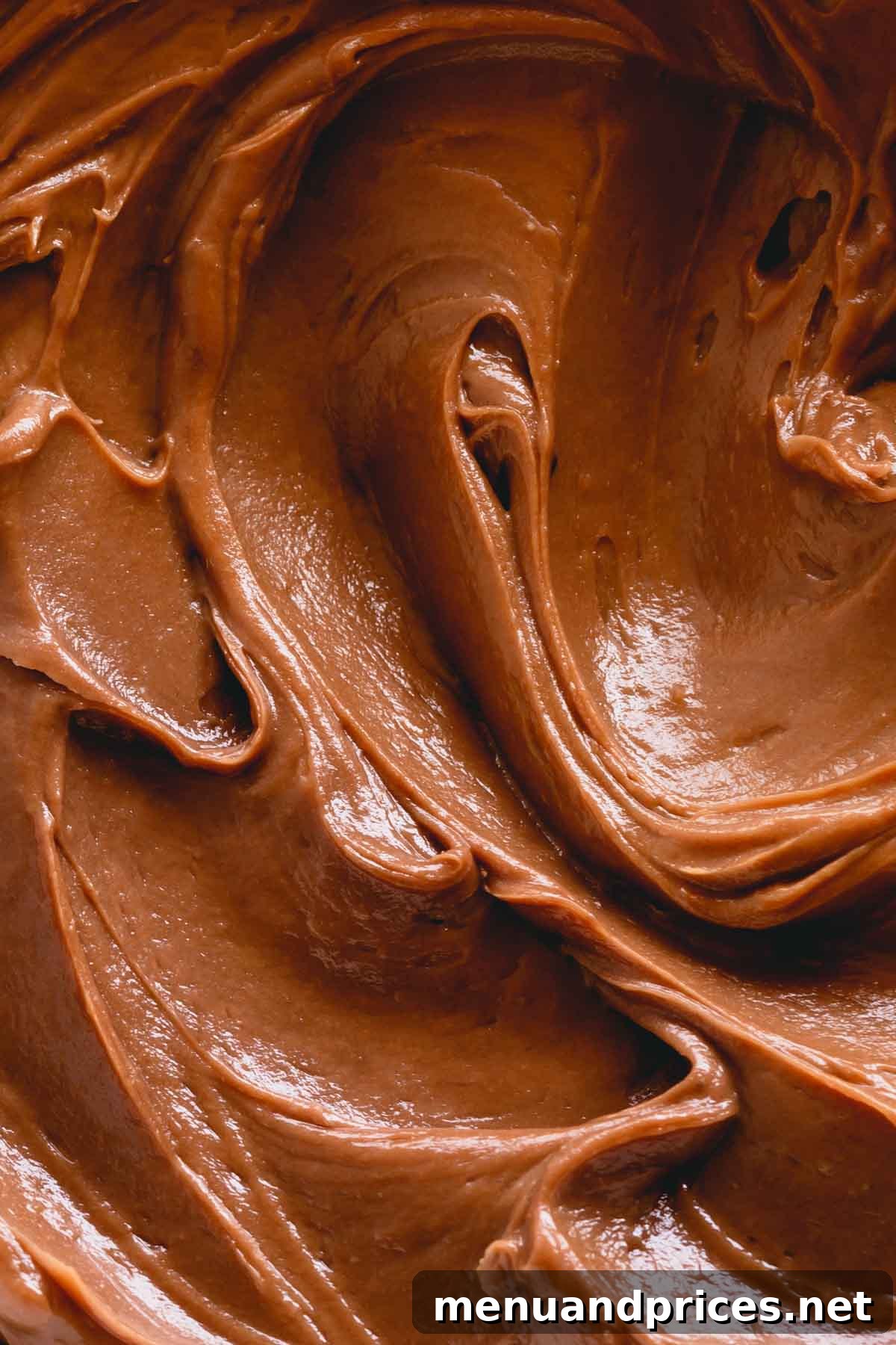 Velvety French Chocolate Frosting 2 Up-close photo of smooth, glossy chocolate buttercream swirling gracefully in a bowl, ready to be piped onto a dessert.