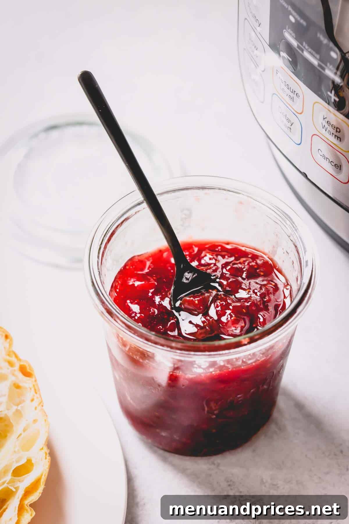 A jar of homemade strawberry jam next to an Instant Pot, signifying ease of preparation.