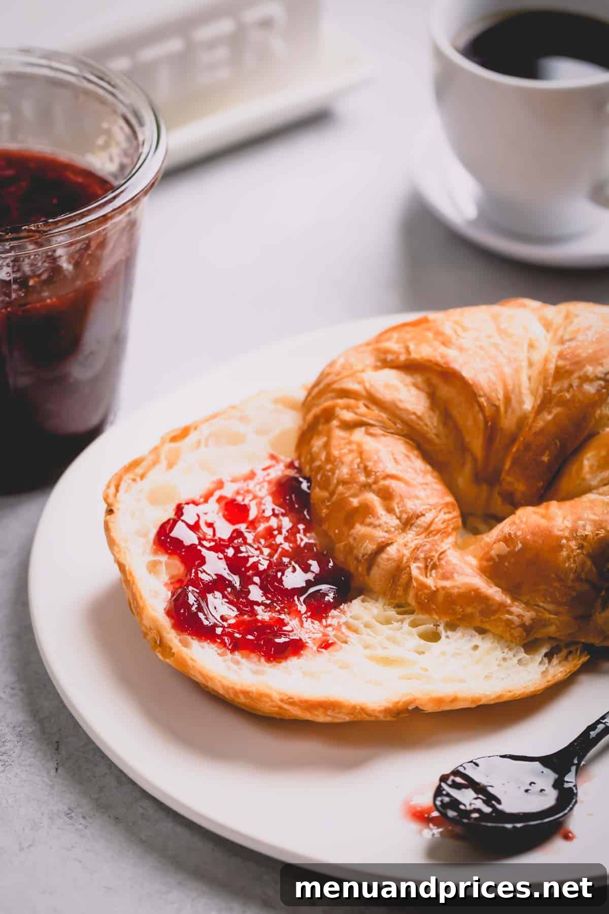 A sliced croissant with a generous spread of homemade strawberry jam.