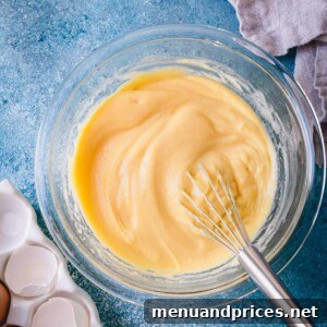 Smooth pastry cream in a glass bowl with a whisk.