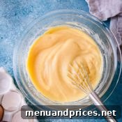 Smooth pastry cream in a glass bowl with a whisk.