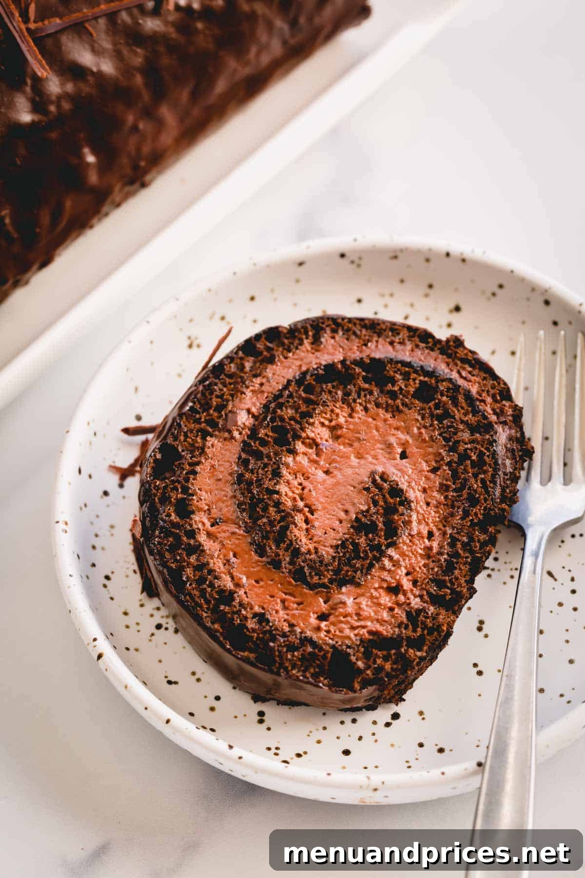 Sinful Chocolate Roll Cake 11 A perfectly cut slice of chocolate roll cake, showcasing the beautiful spiral of fluffy sponge and creamy mousse, elegantly topped with a glossy layer of ganache.