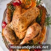 Whole roast turkey on a silver platter garnished with orange slices, pomegranate halves and fresh herbs.