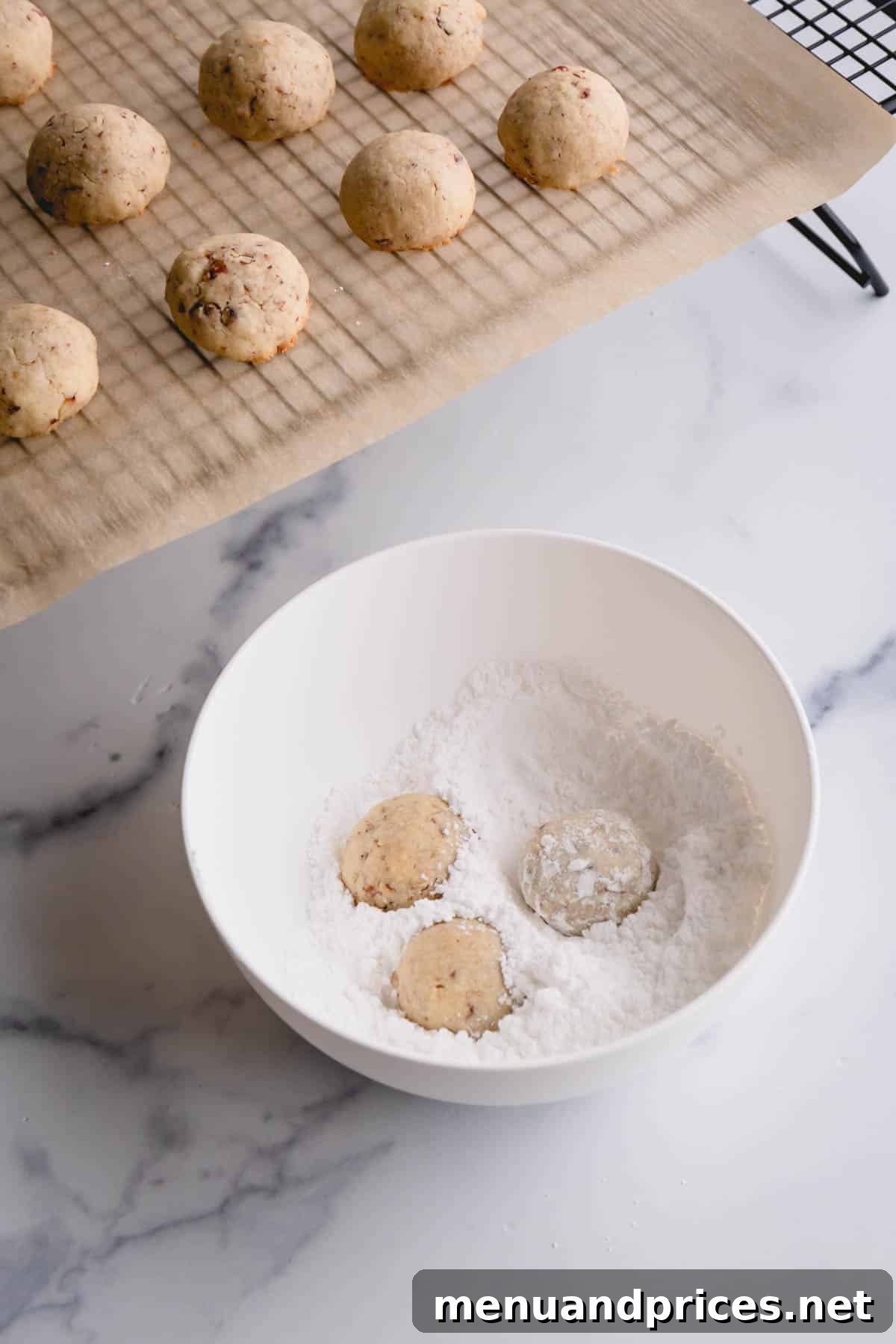 Buttery Pecan Snowball Cookies 12 Warm snowball cookies being rolled in a bowl of powdered sugar for the first coating.