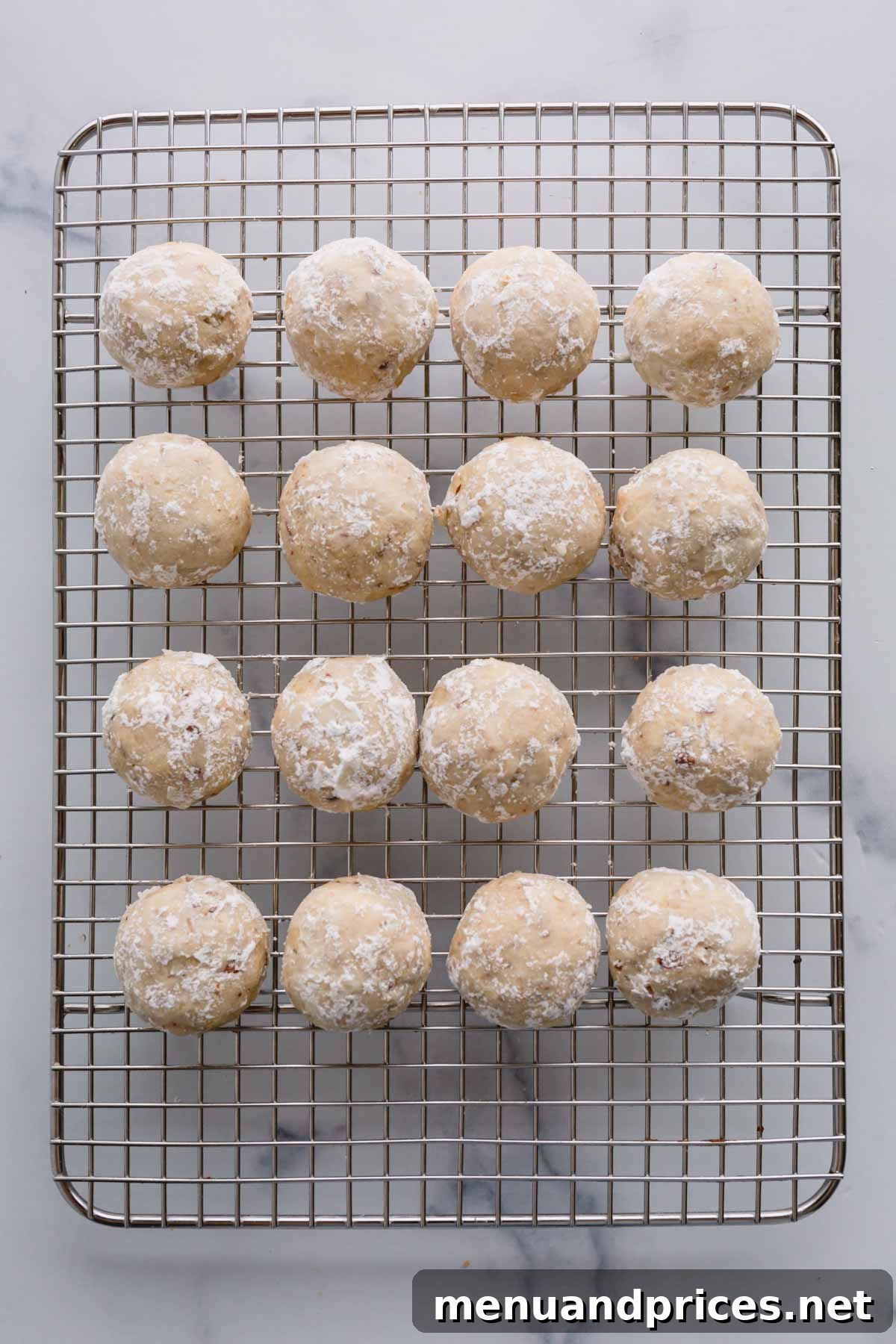 Buttery Pecan Snowball Cookies 13 Snowball cookies that have been rolled once in powdered sugar, arranged on a wire rack.