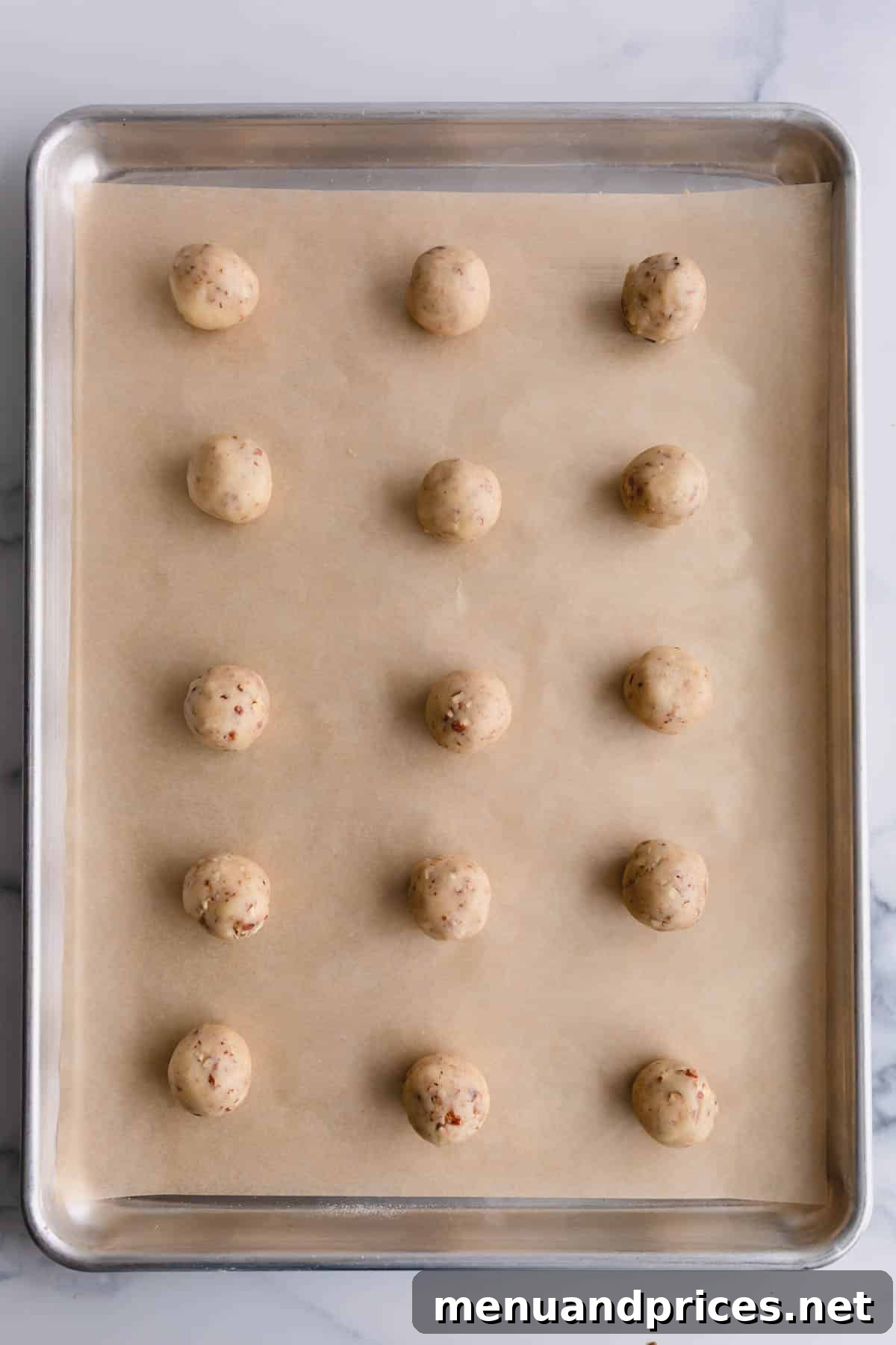 Buttery Pecan Snowball Cookies 9 Unbaked snowball cookie dough balls neatly arranged on a parchment-lined baking sheet.