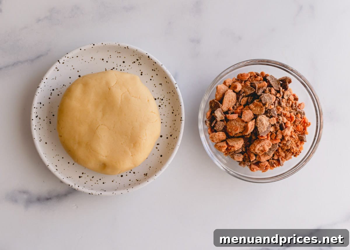 Cookie dough ball and a bowl of butterfinger pieces, ingredients for butterfinger cookies.