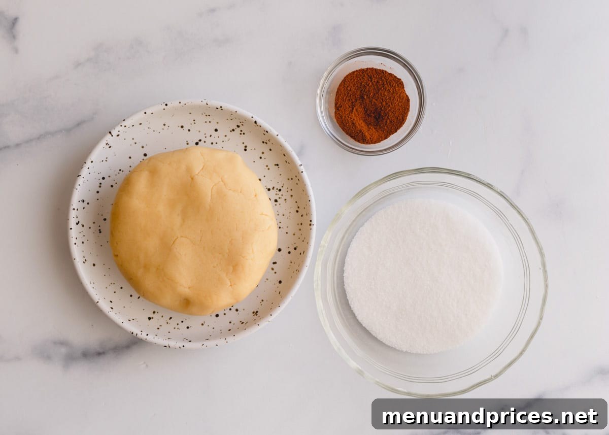 Cookie dough ball and a bowl of ground cinnamon and sugar, ingredients for snickerdoodle cookies.