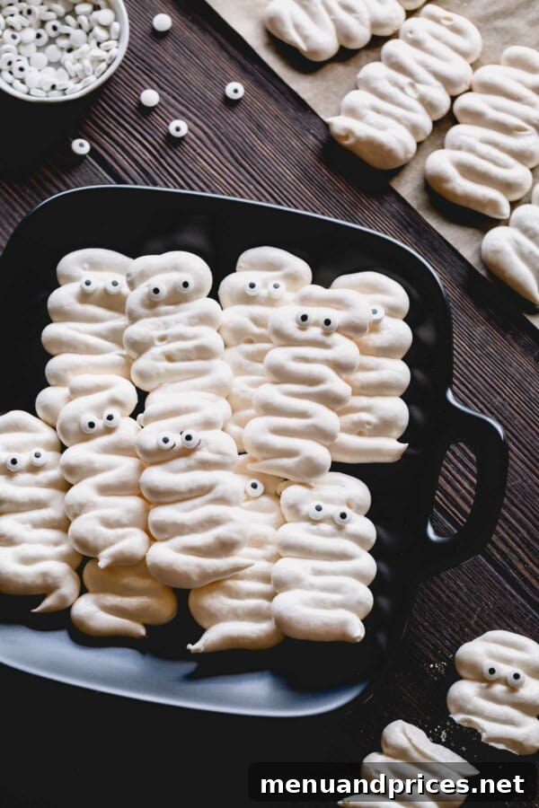 Bandaged Meringue Delights 2 Whimsical mummy meringue cookies with playful googly eyes arranged on a sleek black plate, ready for a Halloween celebration.