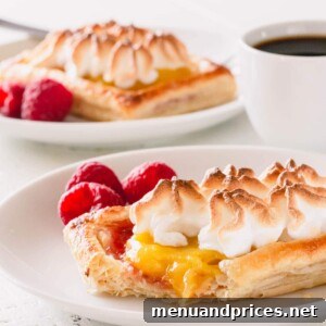 A raspberry lemon meringue tartlet on a white plate with a bite cut off.