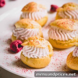 Mini raspberry cream puffs on a white platter dusted with freeze-dried raspberry powder, ready to serve.