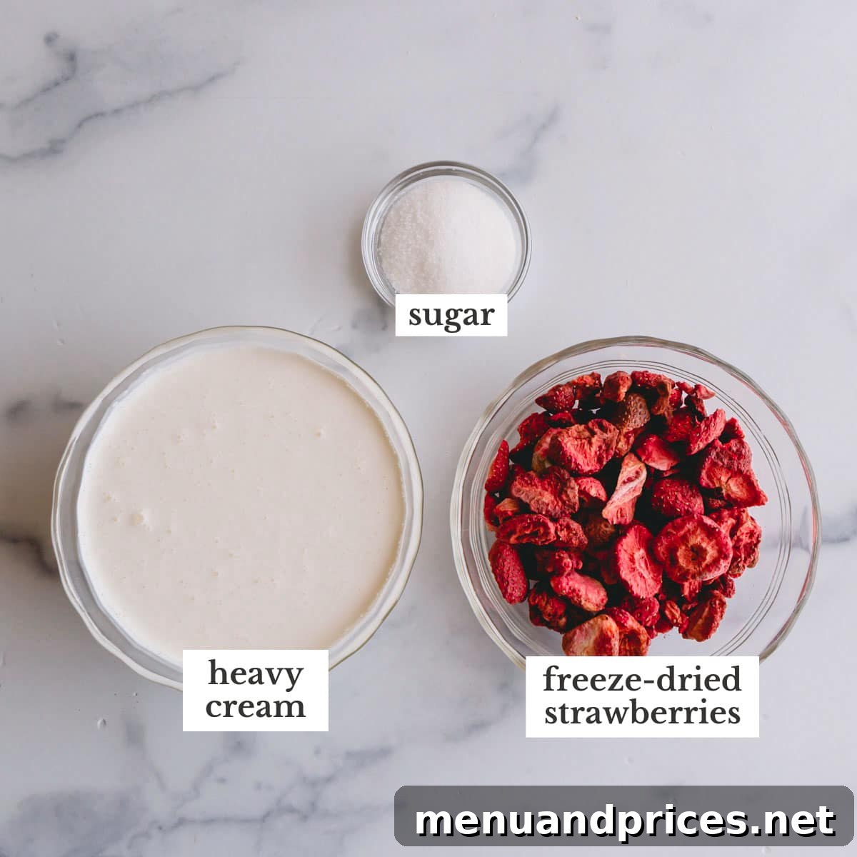 Strawberry Cloud Frosting 4 Overhead image of a bowl of cold heavy cream, a small bowl of granulated sugar, and a bowl of vibrant freeze-dried strawberries.