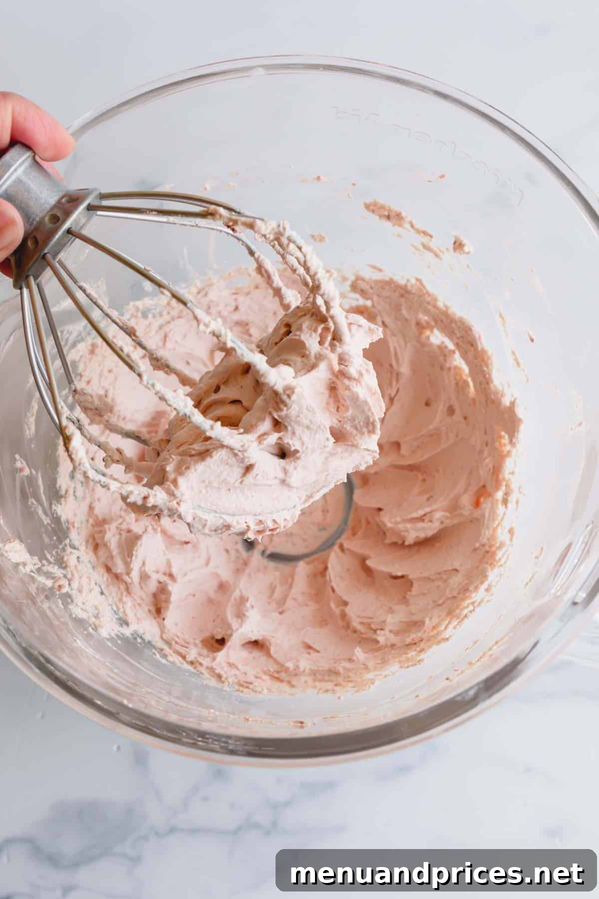 Strawberry Cloud Frosting 7 A whisk being lifted from a bowl of perfectly textured strawberry whipped cream frosting.