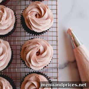 Chocolate cupcakes on a wire rack topped with strawberry whipped cream frosting.