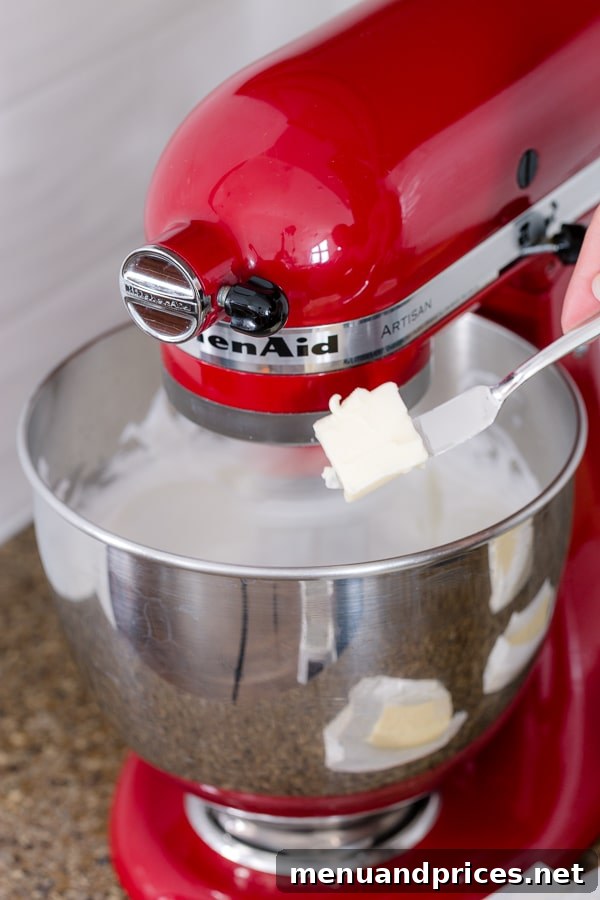 Velvet Strawberry Swiss Buttercream 5 Softened butter being added gradually into a stand mixer with whipped meringue.