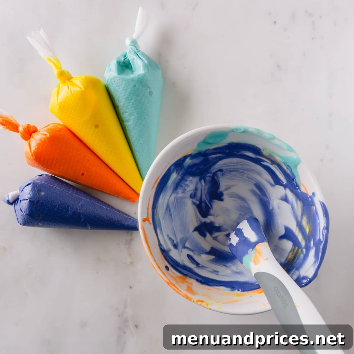 Mastering Royal Icing 8 Piping bags filled with blue, yellow, orange, and purple royal icing, neatly arranged next to a bowl that shows remnants of previous icing colors, demonstrating the one-bowl mixing method.