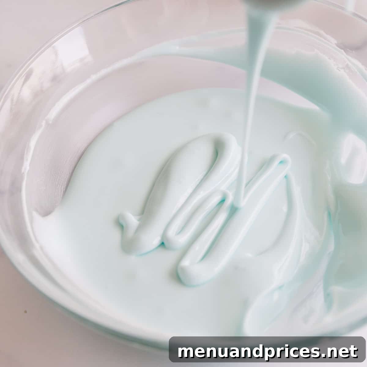 Mastering Royal Icing 9 A bowl of light blue royal icing, with a spatula lifting some icing to demonstrate the desired hybrid consistency.