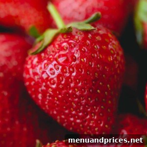 A bowl of fresh strawberries next to a jar of white vinegar and water, demonstrating the cleaning process.