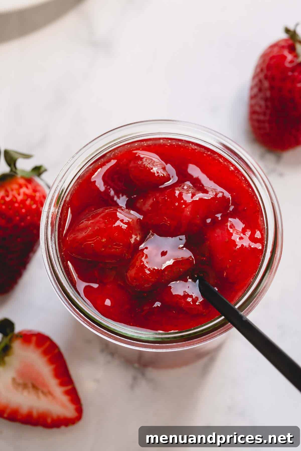 Whip Up Perfect Strawberry Sauce 6 Overhead image of a spoon sticking out of a glass jar full of chunky strawberry sauce, ready to be enjoyed.