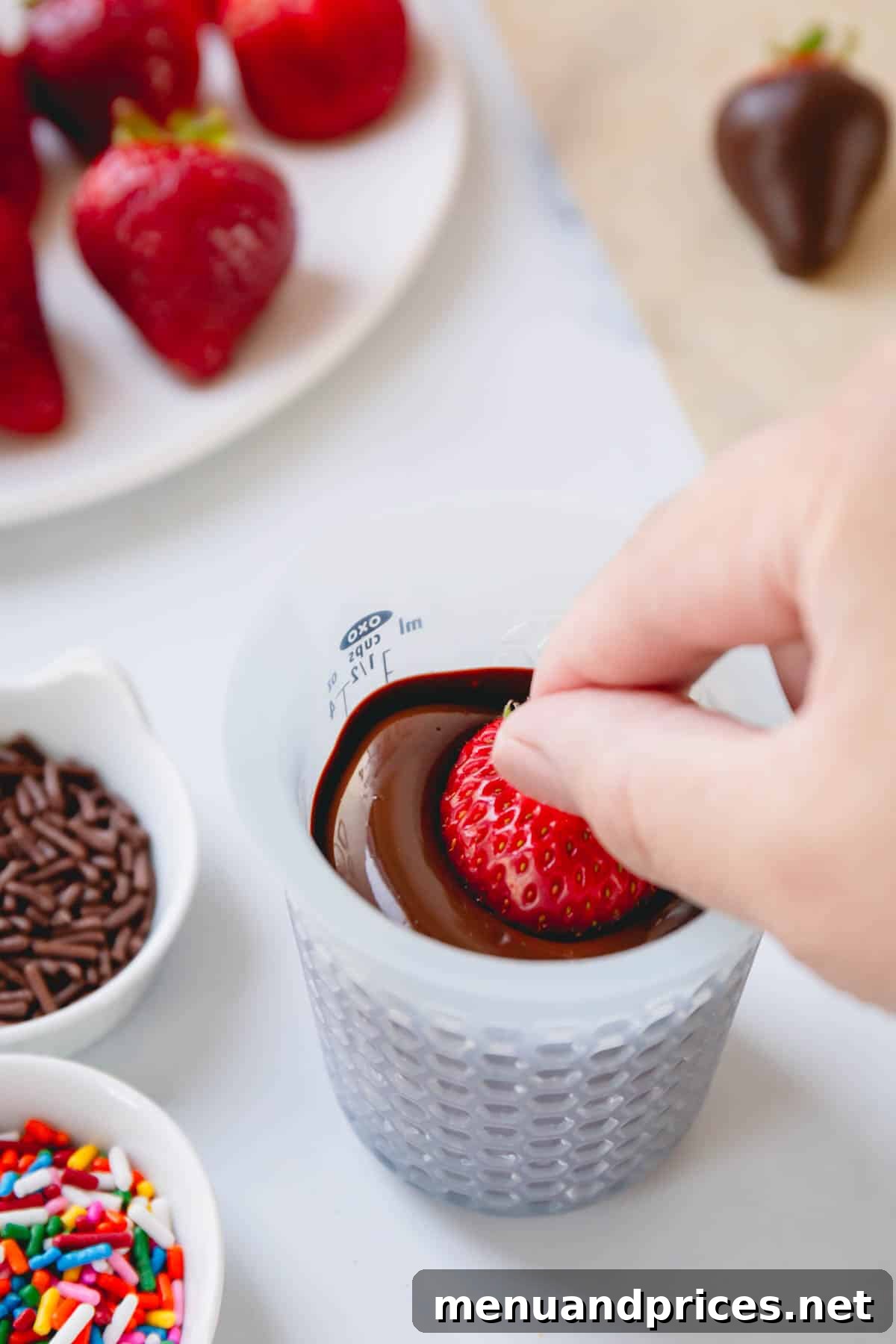 Gourmet Chocolate Strawberries 7 A hand dipping a clean strawberry into melted chocolate.