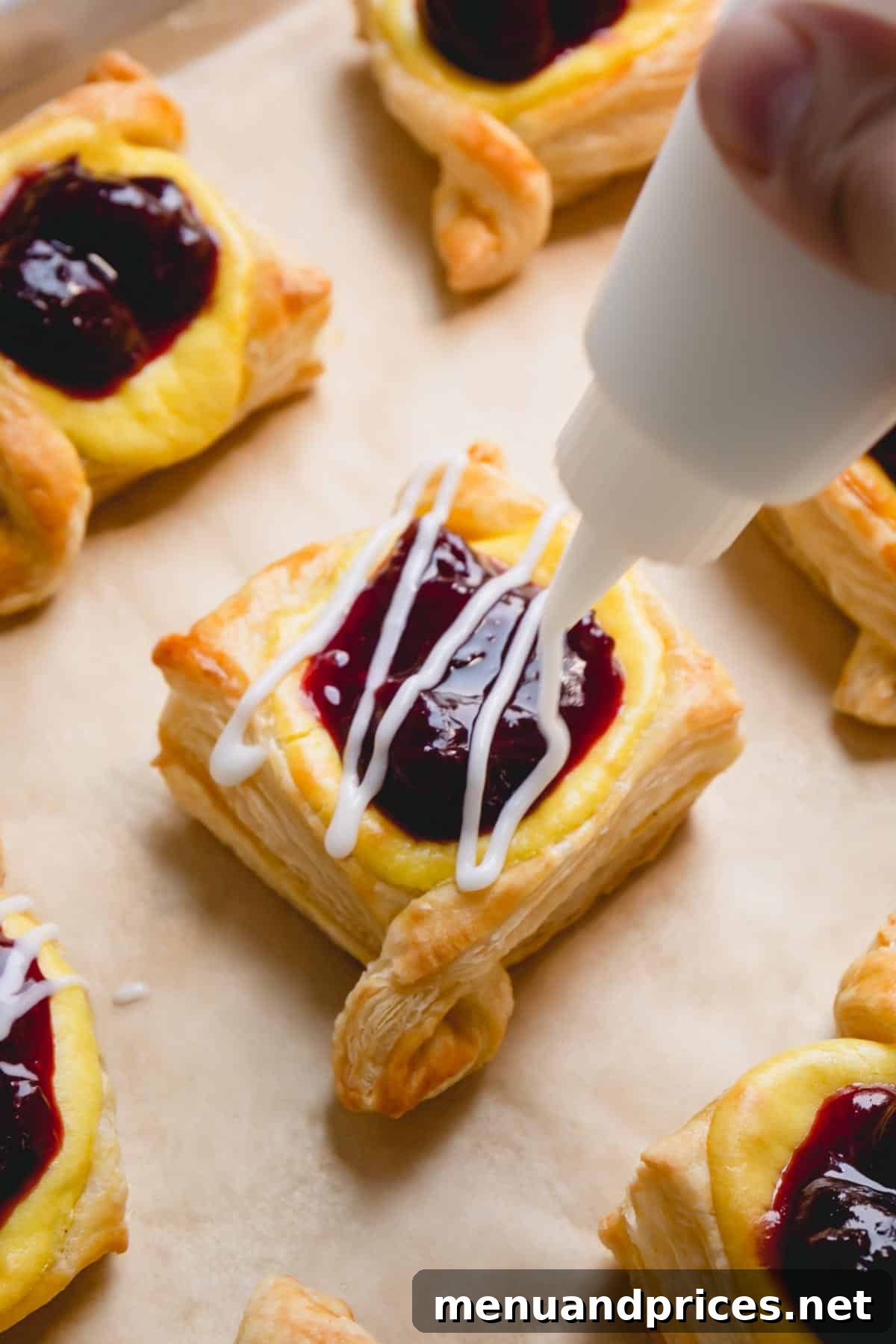 A delicate stream of powdered sugar glaze being artfully piped over a warm, baked cherry danish on a baking sheet, creating a beautiful finish.