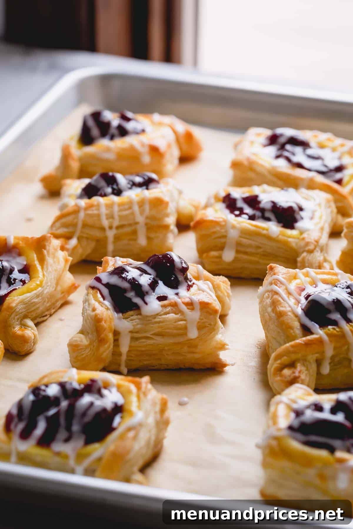An appetizing side view of multiple cherry danishes, each generously topped with a sweet powdered sugar glaze, perfectly arranged on a parchment paper-lined baking sheet.