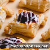 A closeup of a baked cherry cheese danish on a parchment paper-lined baking sheet, glistening with glaze.