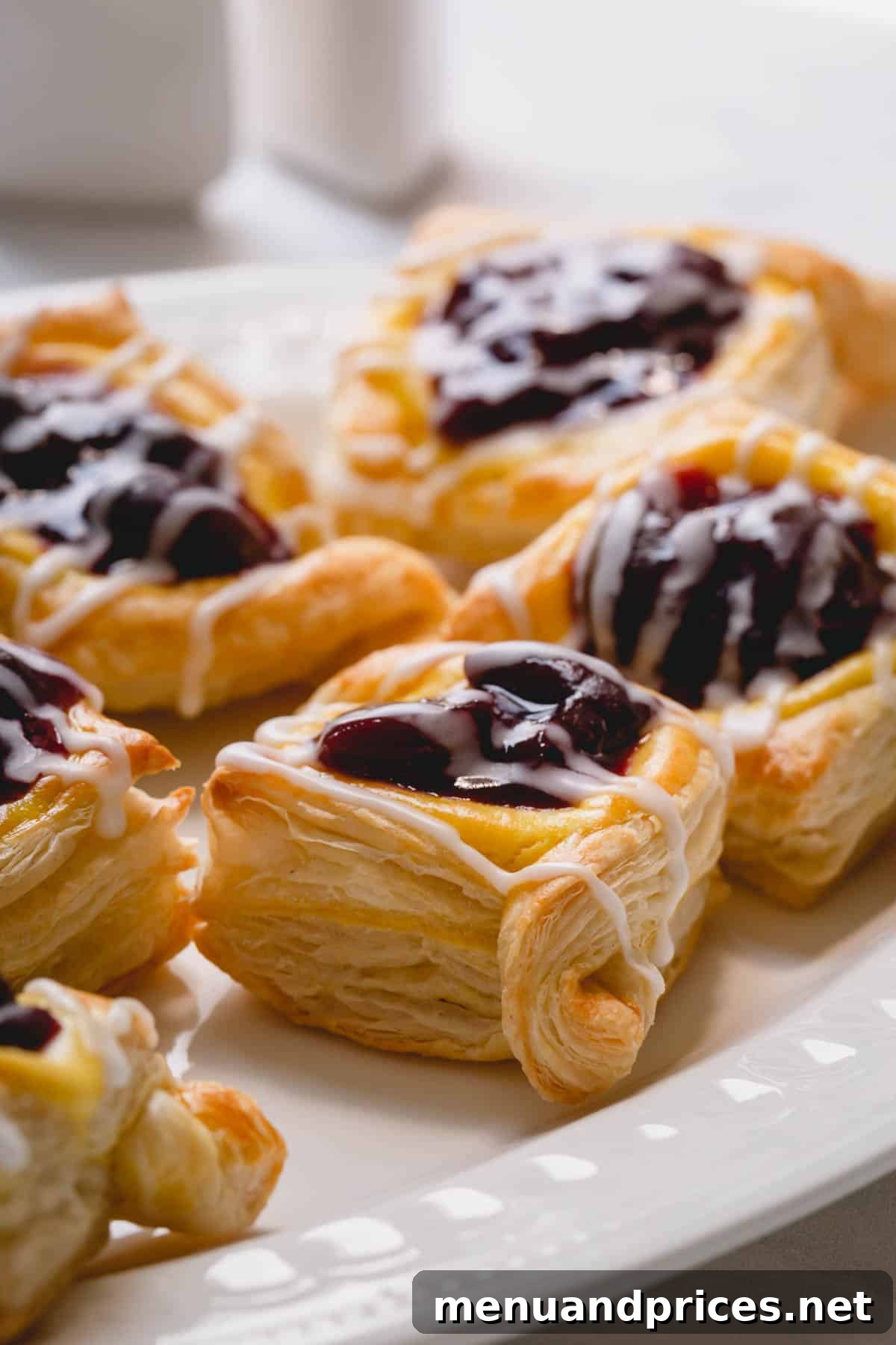 Beautifully arranged cherry danishes, glistening with a powdered sugar glaze, presented on a white plate ready to be served.