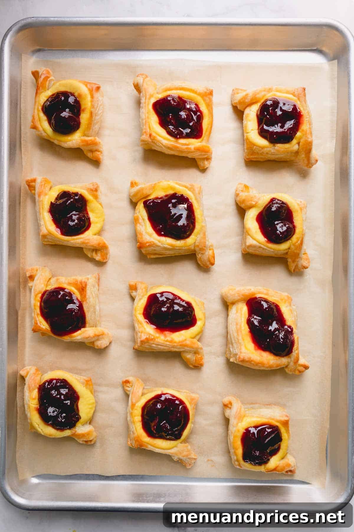 A parchment paper-lined baking sheet showcasing 12 delectable cherry cheese danishes, beautifully assembled and awaiting the final glaze.