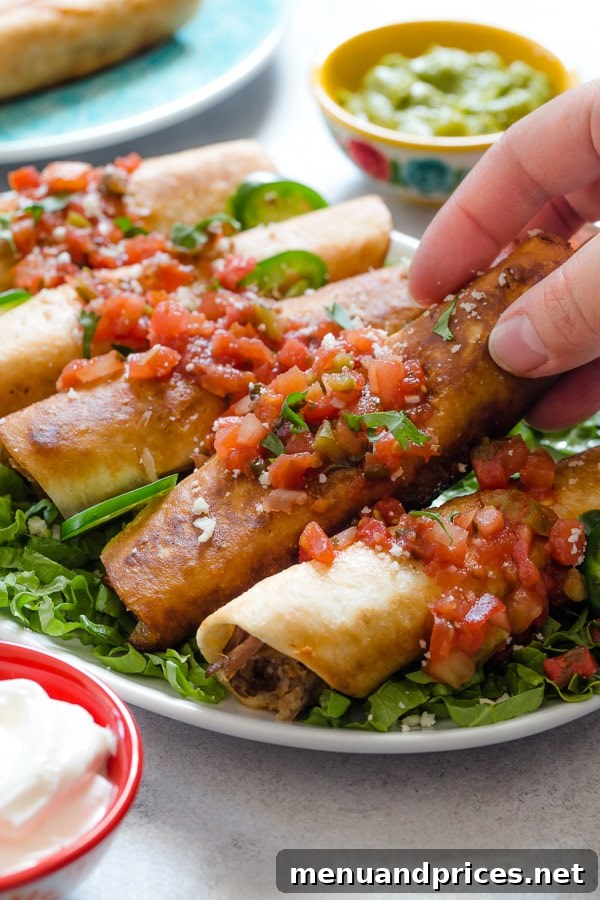 A hand grabbing a golden-brown pulled pork flauta topped with fresh pico de gallo from a vibrant plate, highlighting its crispy texture.