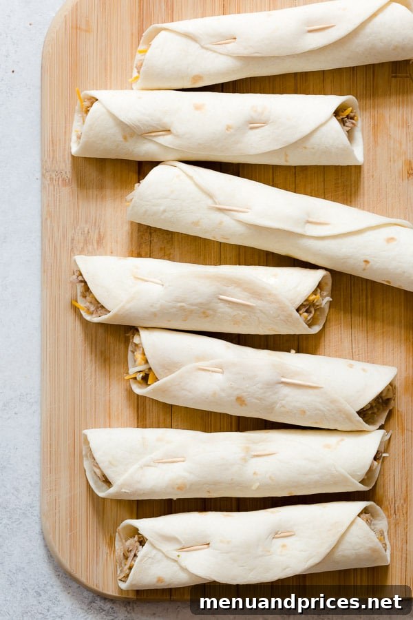 Several uncooked pulled pork flautas, neatly rolled and secured with toothpicks, lined up on a surface ready for frying.