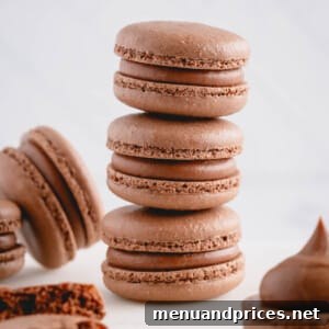 Three filled chocolate macarons stacked on top of each other surrounded by other chocolate macarons.