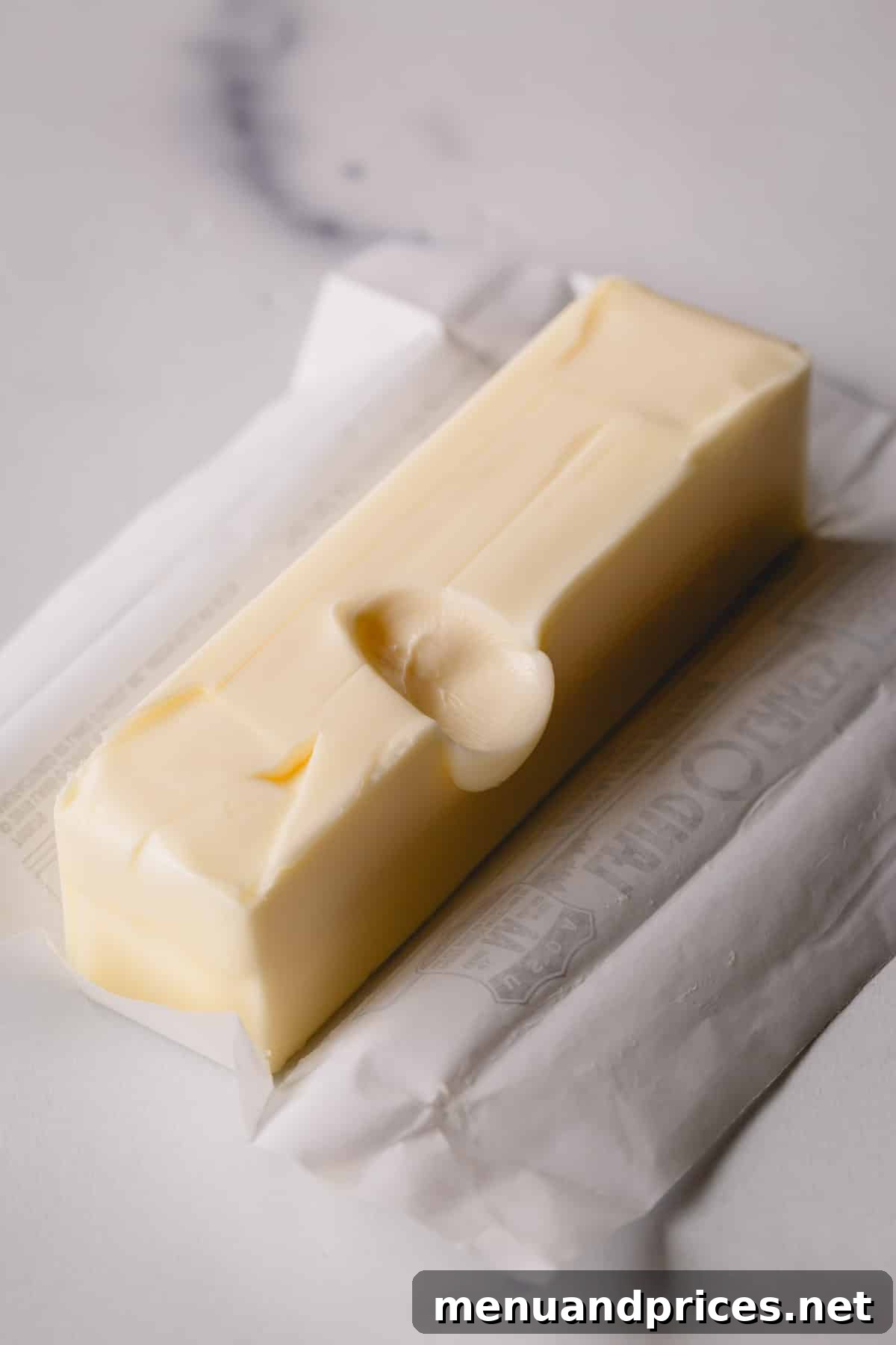 A stick of unwrapped butter featuring a clear finger indent in its center, perfectly demonstrating the 'finger test' for ideal softness.