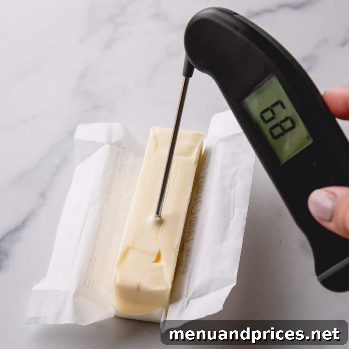 A stick of butter with an instant-read thermometer precisely inserted, displaying a reading of 68°F, indicating the optimal temperature.