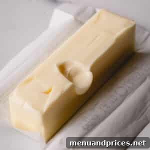 A stick of unwrapped butter with a finger dent in the middle, ready for baking.