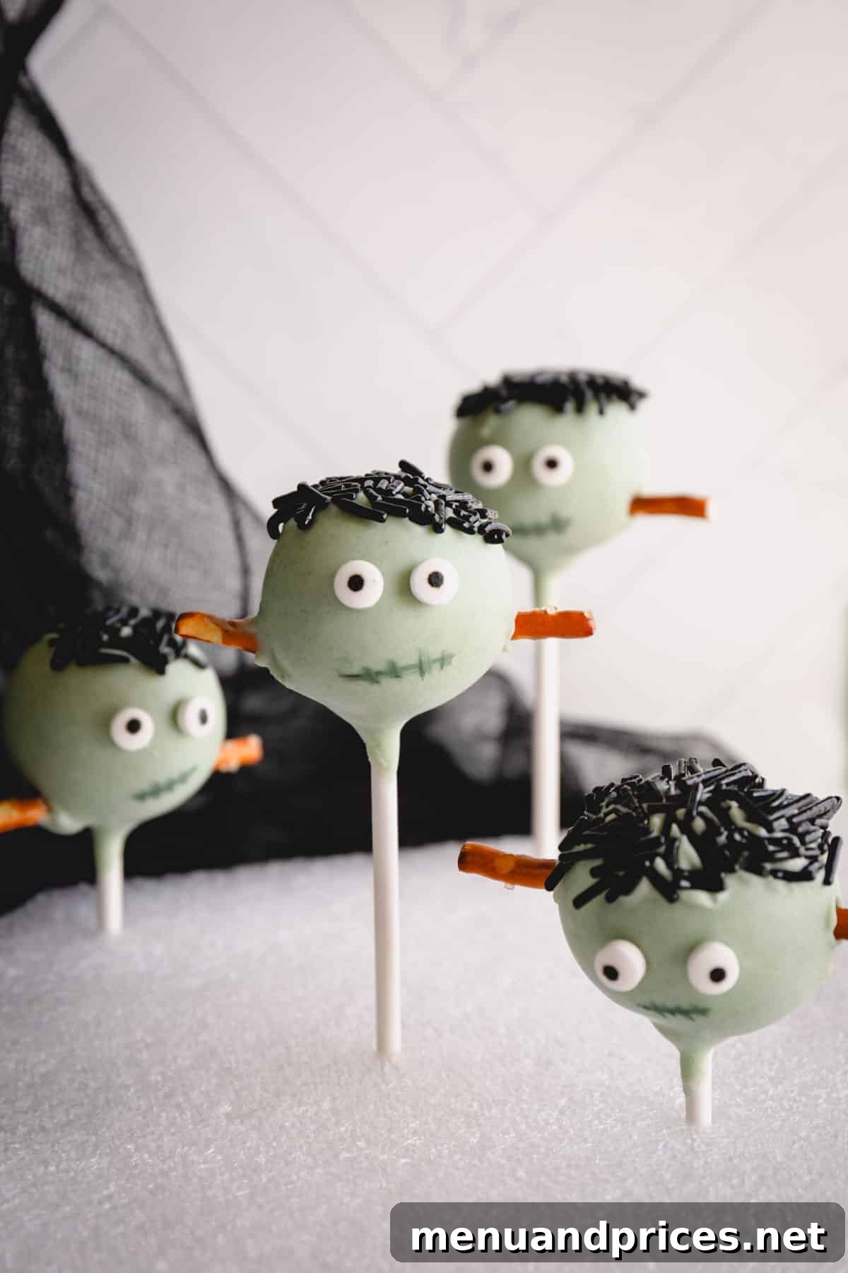 Close-up of Frankenstein Halloween cake pops with green coating, black sprinkles for hair, pretzel stick bolts, and candy eyes.