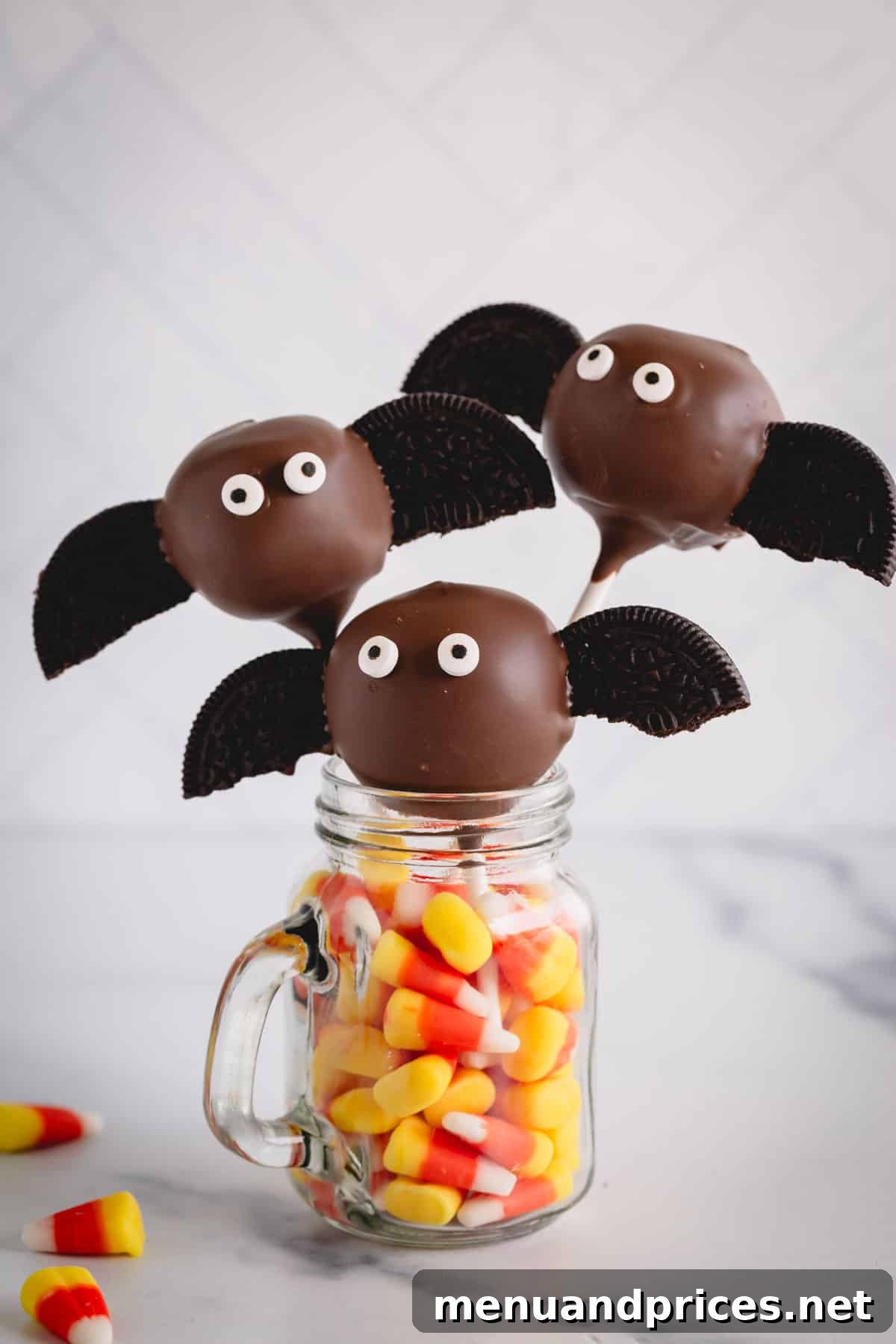 Bat cake pops with Oreo wings and candy eyes, artfully displayed in a mason jar filled with candy corn.
