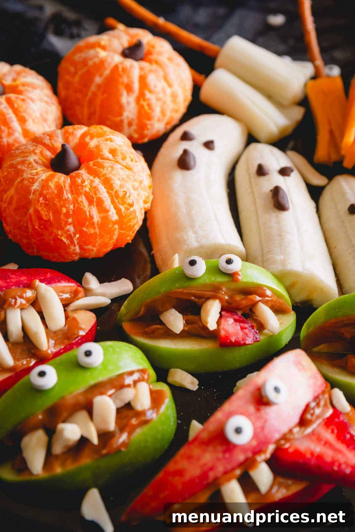 Close-up of a Halloween snack board showing pumpkin oranges, banana ghosts, and apple monster mouths.