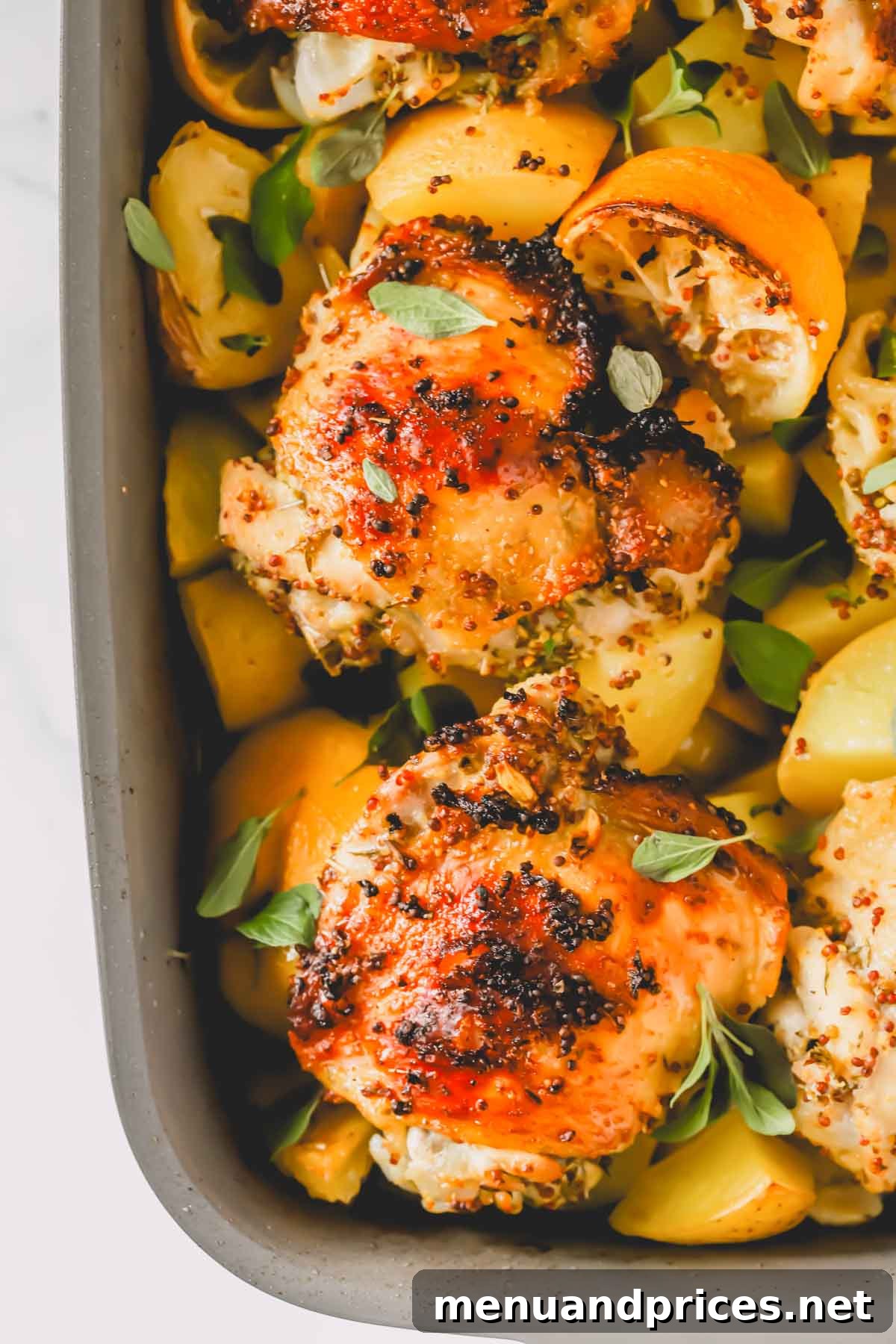 A close-up of golden-brown Greek lemon chicken pieces nestled among roasted potatoes and lemon halves in a baking dish, fresh out of the oven.