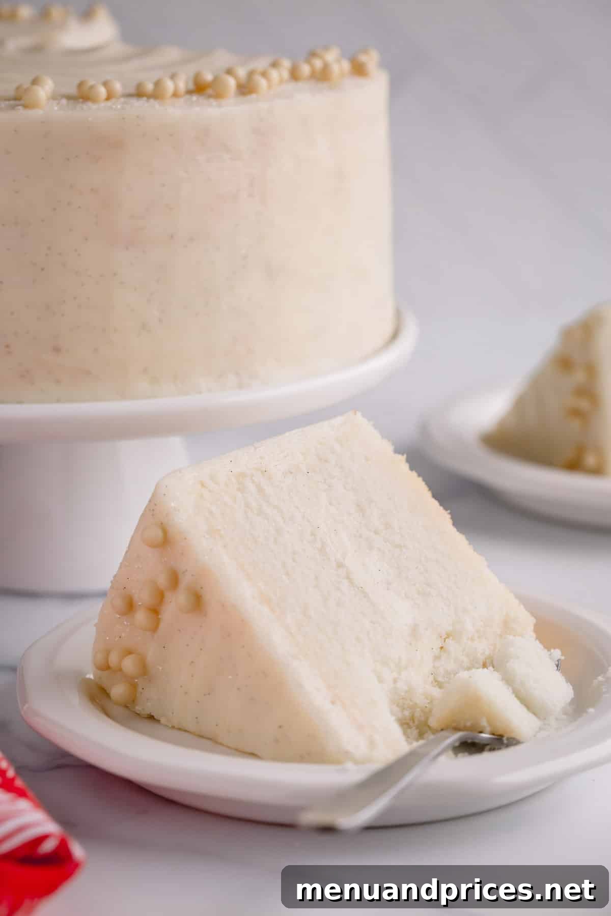 Fluffy White Cake Perfection 14 A beautiful slice of classic white cake on a plate, with a fork gently taking a piece, and the complete frosted cake visible in the background.