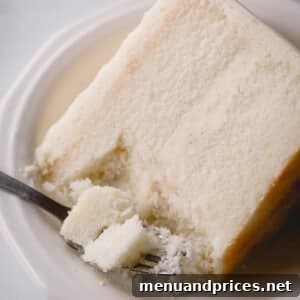 A slice of white cake on a plate with a fork taking a bite, zoomed in to show detail.