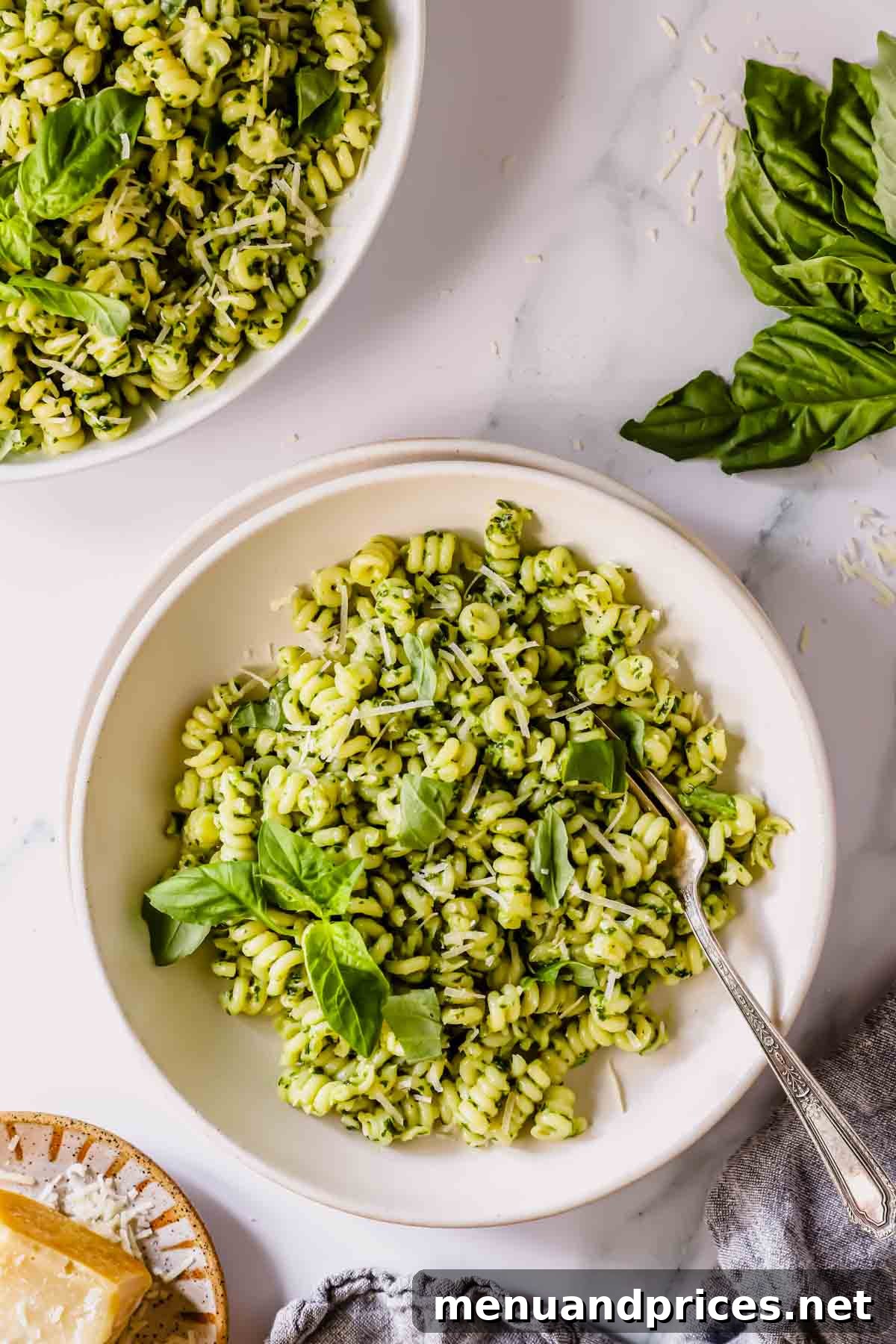 A bowl of basil pesto pasta with a fork and a second bowl of pasta to the side.