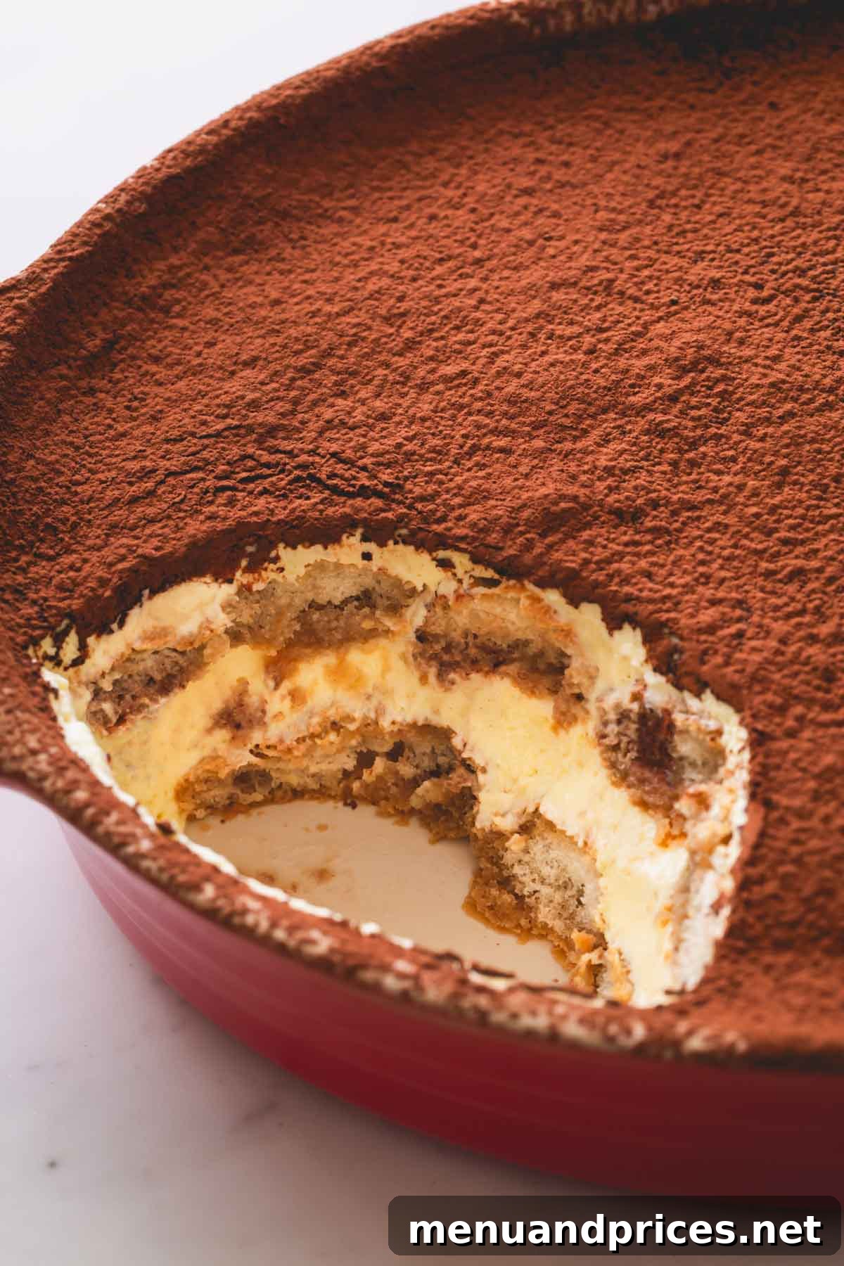 Authentic Italian Tiramisu 13 A large rectangular dish of classic tiramisu, with a generous portion having been scooped out, showcasing the distinct layers of ladyfingers and mascarpone cream, topped with cocoa powder.
