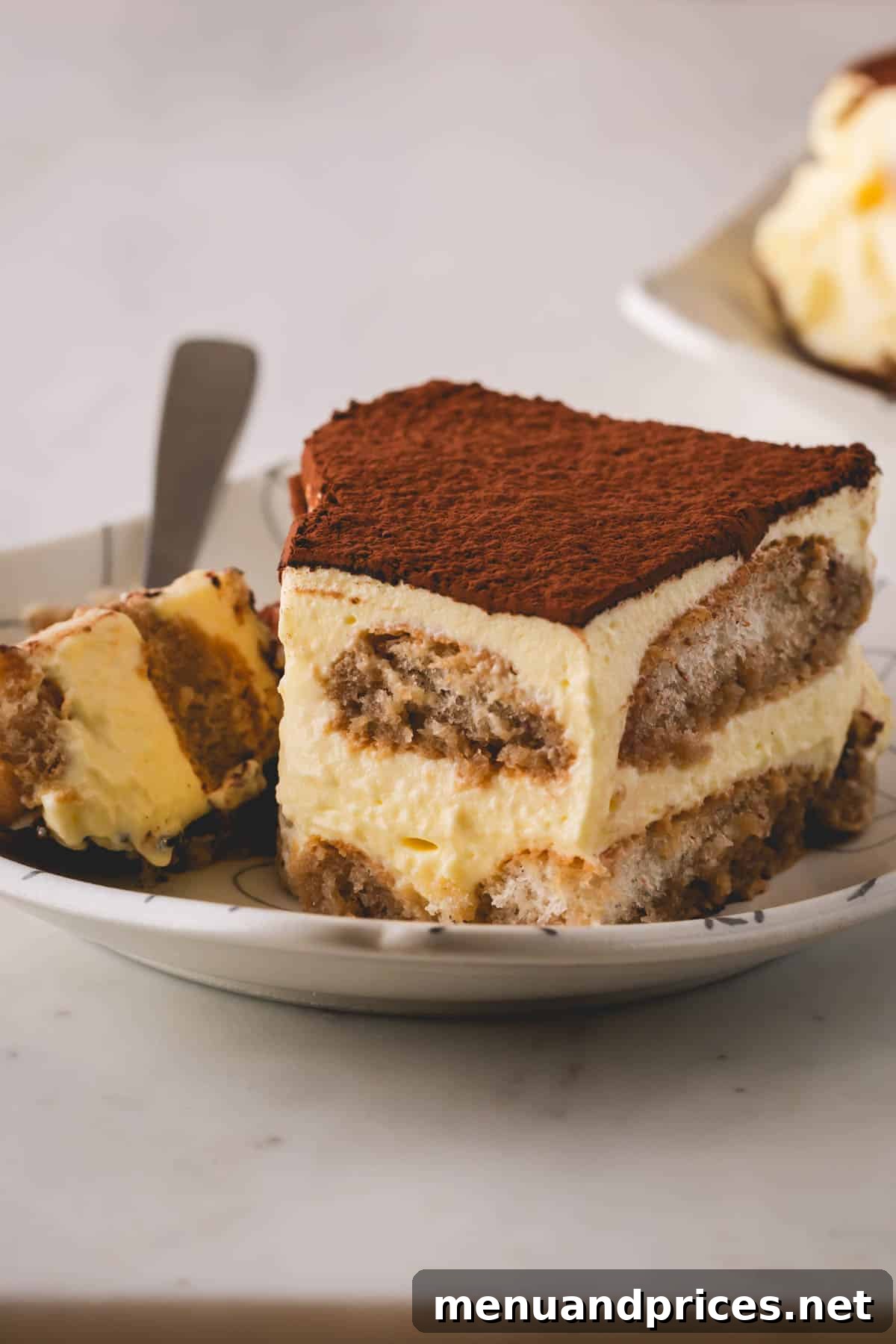 Authentic Italian Tiramisu 15 A perfect square slice of classic tiramisu, exquisitely plated, with a fork gently taking a corner bite, showcasing the moist ladyfingers and creamy filling, topped with cocoa powder.