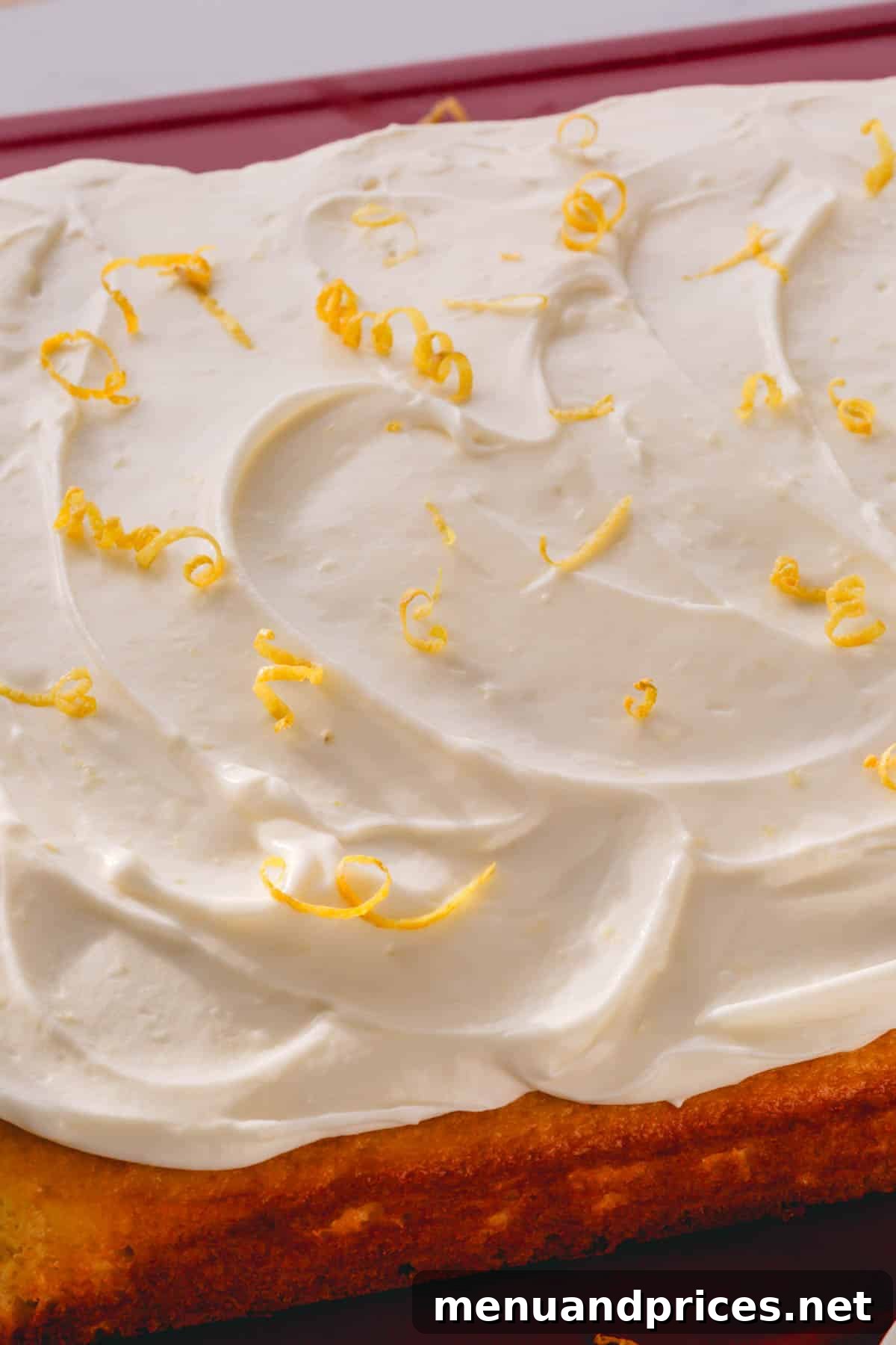 A vibrant yellow cake topped with generous swirls of lemon cream cheese frosting and elegantly curled lemon zest.
