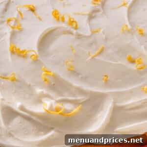 A yellow cake topped with lemon cream cheese frosting and lemon zest curls.