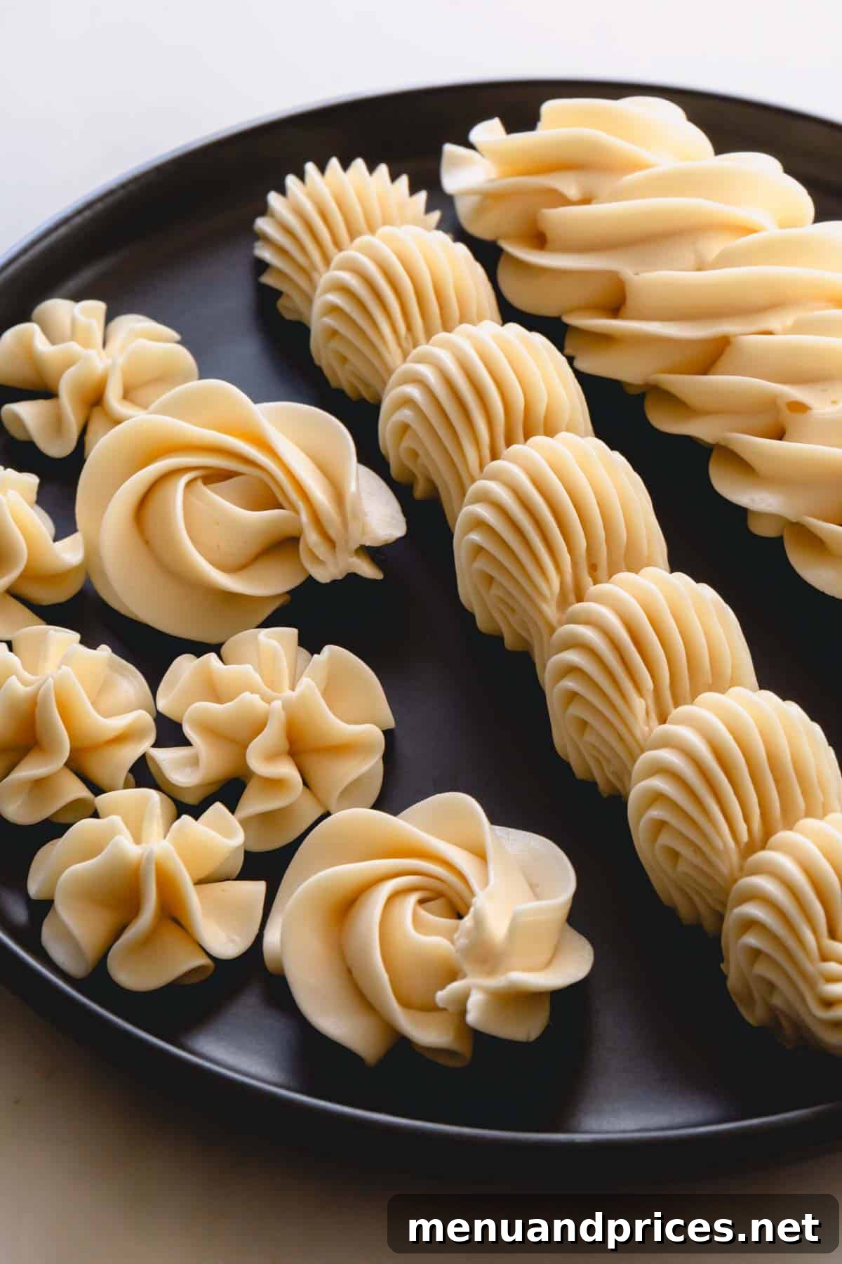 Classic Vanilla Russian Buttercream 8 Exquisite piped designs of vanilla Russian buttercream presented on a sleek black plate, highlighting its elegant finish and stable form.