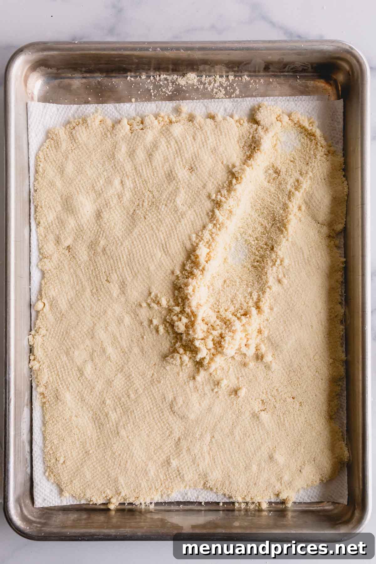 Mastering Dry Almond Flour: From Oily to Optimal 8 A layer of perfectly dried almond flour on a baking sheet, with a spoon fluffing some of it, showcasing its improved light and airy texture.